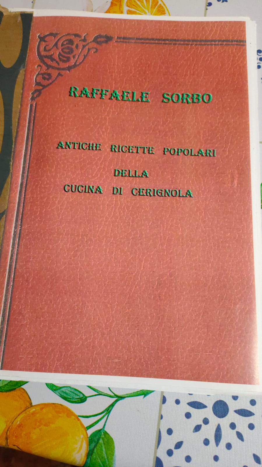 Copertina del libro "Antiche Ricette Popolari della Cucina di Cerignola" di Raffaele Sorbo. Il volume presenta una veste grafica classica con uno sfondo che simula la pelle rossa e titoli in verde, arricchita da un fregio decorativo nero nell'angolo superiore sinistro.