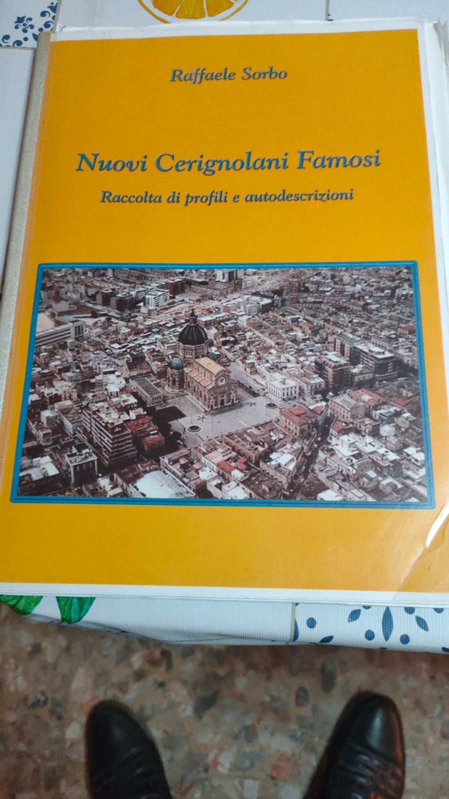 Copertina del libro "Nuovi Cerignolani Famosi - Raccolta di profili e autodescrizioni" di Raffaele Sorbo. Su sfondo giallo è presente una fotografia aerea della città di Cerignola, che mette in evidenza la maestosa cupola del Duomo Tonti al centro.